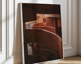 May include: A photograph of a building's interior with a curved, orange-colored staircase. The staircase is lit by natural light coming from a window.