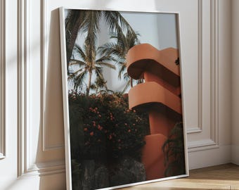 May include: A framed photograph of a modern building with a curved facade, surrounded by lush tropical foliage. The building is painted in a warm orange hue, and the palm trees are silhouetted against a bright blue sky.