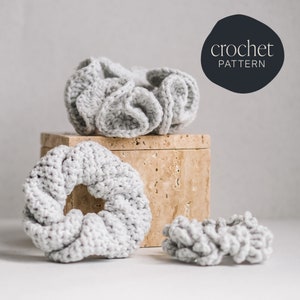 Puede incluir: Tres scrunchies de pelo de crochet gris, uno en una caja de piedra beige y dos en una superficie blanca. Los scrunchies están hechos con un punto texturizado. La imagen incluye el texto "crochet pattern".