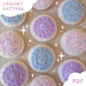 Può includere: Un modello di uncinetto in PDF che mostra diversi biscotti circolari lavorati all'uncinetto con basi bianche e cime color blu pastello, rosa o viola, decorate con piccoli zuccherini di filato multicolore. Include grafiche a stella.