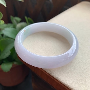 Op de afbeelding: Een gladde, gepolijste armband gemaakt van doorschijnende witte steen met een subtiele zweem van lichtgroene kleur. Het cirkelvormige accessoire heeft een afgerond buitenprofiel en een glanzende afwerking die het licht over het oppervlak weerkaatst.