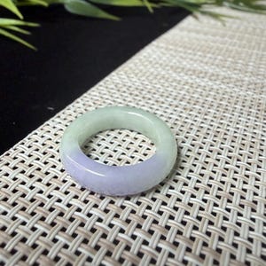 May include: A smooth, circular ring crafted from polished stone, featuring a distinct color gradient that transitions from a pale, translucent mint green on the upper portion to a soft, muted lavender purple on the lower half of the band.