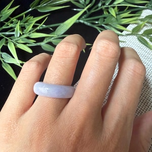 May include: A smooth, solid band ring crafted from light lavender-colored stone. The ring features a rounded, polished surface with a consistent thickness throughout the entire circumference, showcasing a soft, pale purple hue and a natural finish.
