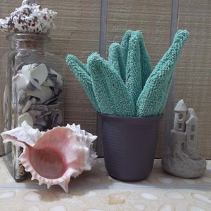 May include: A green and blue fabric plant in a gray pot, next to a glass jar filled with seashells, a pink seashell, and a gray concrete castle.