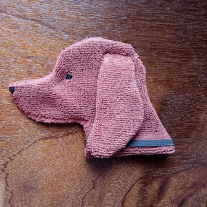 May include: A brown plush dog toy with black eyes. The toy has a black elastic band around the neck.