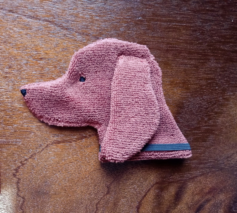 May include: A brown plush dog toy with black eyes. The toy has a black elastic band around the neck.