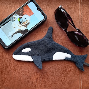 May include: A black and white plush orca whale toy with a white belly and a black back. The toy is lying on a brown leather surface.