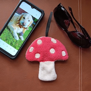 May include: A red and white plush mushroom toy with white polka dots. The mushroom is on a brown leather surface.