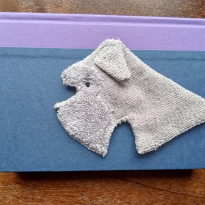 May include: A gray plush dog bookmark with a blue and purple book in the background.