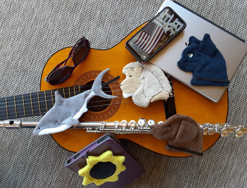 This is a group photo of different Smudge products that are available:  a shark, a lion, sunflower, black cat and chocolate lab. They are arranged with different items that they can be used to clean and polish: a guitar, a flute, tablet, etc.