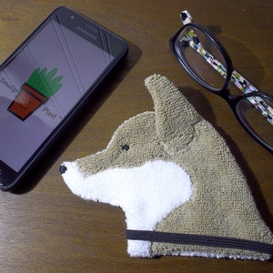 Showing scale of Smudge Dog with two of the many items it can clean and polish: smart phone and eye glasses.