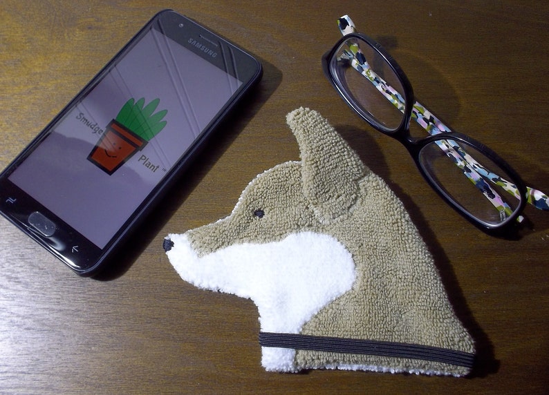 Showing scale of Smudge Dog with two of the many items it can clean and polish: smart phone and eye glasses.