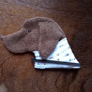 May include: A brown plush dog toy with a white and brown patterned fabric bib. The bib has a black elastic band.