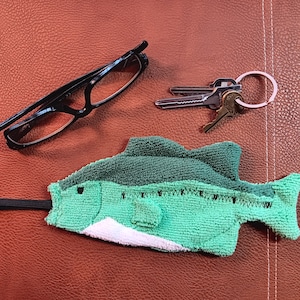 May include: A green and white fish-shaped tea towel with a black string attached. The tea towel is made of a soft, absorbent material and is ideal for drying dishes or wiping down surfaces.