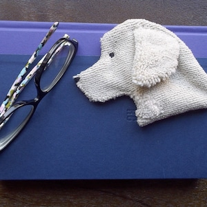 May include: A blue hardcover journal with a white, fluffy dog-shaped bookmark on top. The bookmark has a black eye and is made of a soft, textured material.