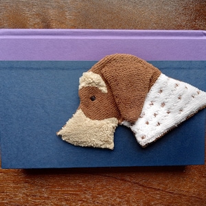 May include: A brown and white plush dog toy with a blue and purple book in the background.