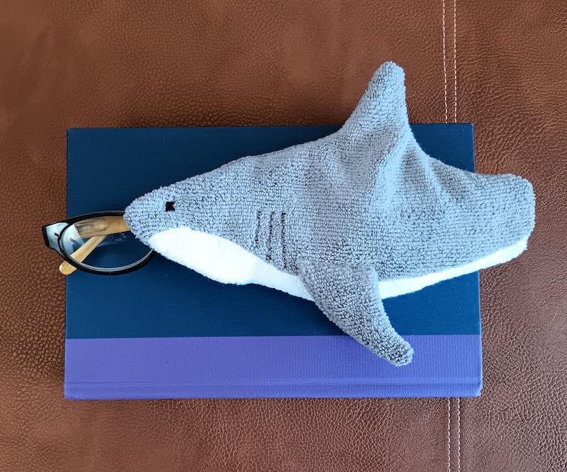 Shark shaped glasses case holding glasses on top of book