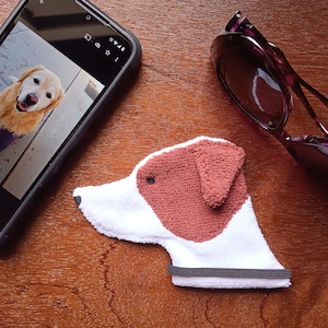 May include: A white and brown plush dog hand puppet with a black elastic band around the wrist. The puppet has a brown nose and brown ears.