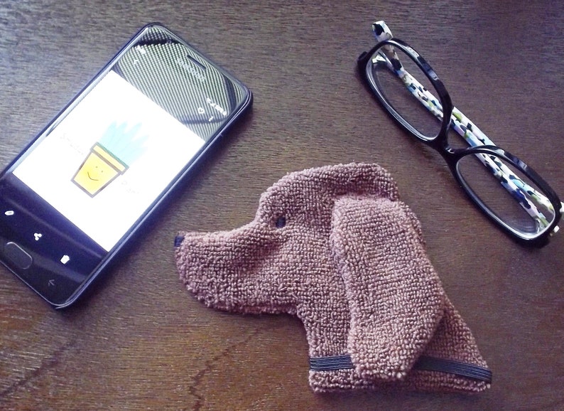 Showing scale of Smudge Dog with two of the many items it can clean and polish: smart phone and eye glasses.