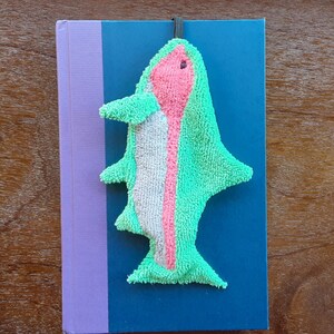 Smudge Fish has a ¼ inch braided elastic loop that can be used as a bookmark. This picture shows the Rainbow Trout being used as a bookmark on a hard backed book.