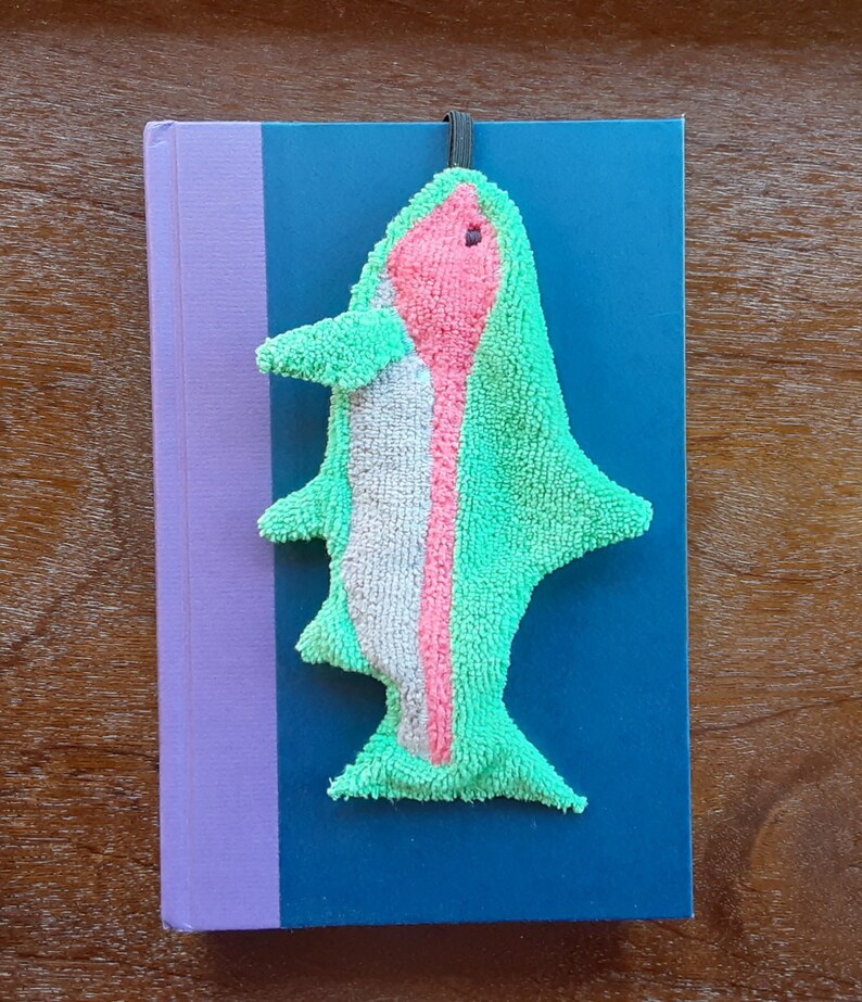 Smudge Fish has a ¼ inch braided elastic loop that can be used as a bookmark. This picture shows the Rainbow Trout being used as a bookmark on a hard backed book.