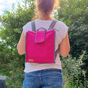 May include: A pink backpack with grey straps and a small pocket on the front. The backpack has a label that says "The Handmade Home".