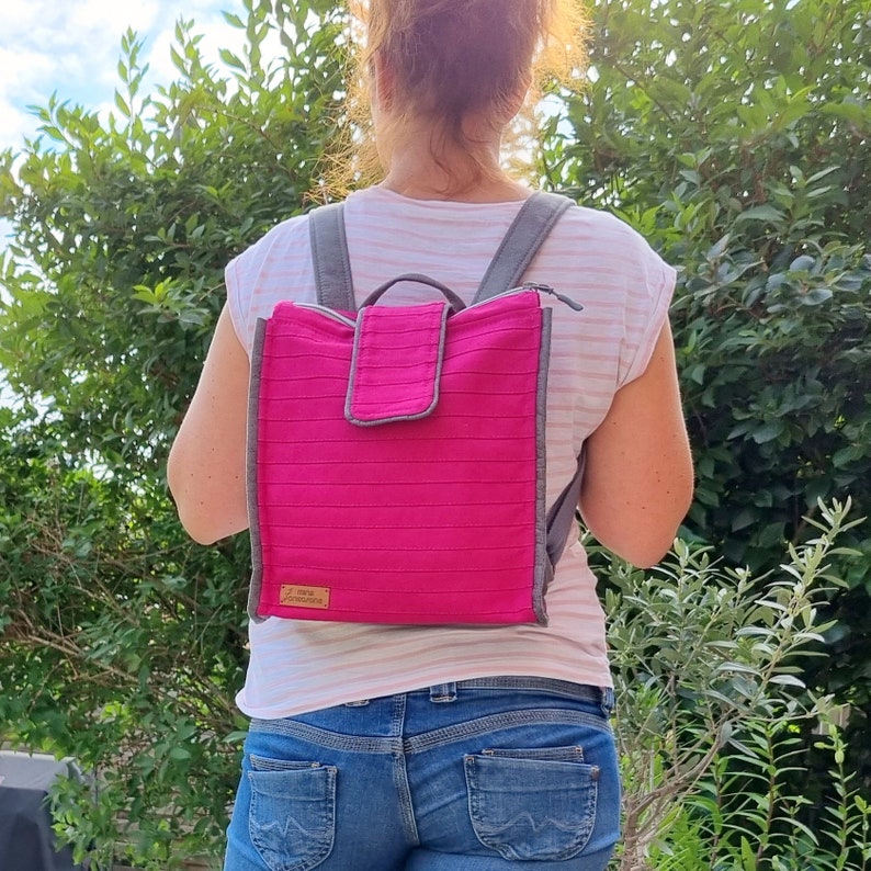 May include: A pink backpack with grey straps and a small pocket on the front. The backpack has a label that says "The Handmade Home".