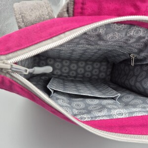 May include: The inside of a pink zippered bag with a grey patterned lining. The bag has a small zippered pocket on the inside.