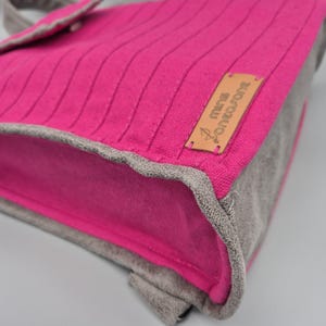May include: A pink canvas bag with a brown leather patch that says "MANU METROPOLA". The bag has a grey suede trim.