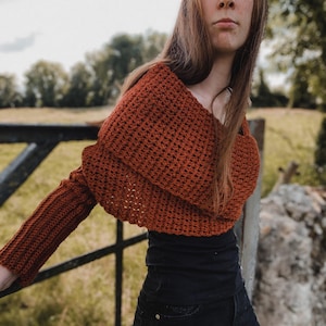 May include: A burnt orange crocheted bolero with long sleeves. The open-front design has a wide, folded collar and a textured stitch pattern. The garment is made of a soft, warm material, ideal for layering.