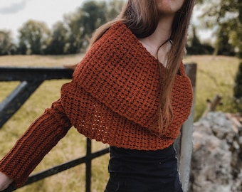 May include: A rust-colored, crocheted shrug with long sleeves. The open-front design features a wide, folded collar and a textured stitch pattern. The garment is made of a soft, warm material, perfect for layering.