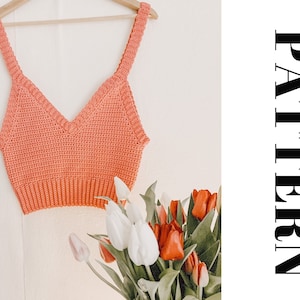 Könnte beinhalten: Ein Korallen-Crochet-Top mit V-Ausschnitt. Das Top ist mit einem einfachen Stichmuster gearbeitet und hat eine verkürzte Länge.