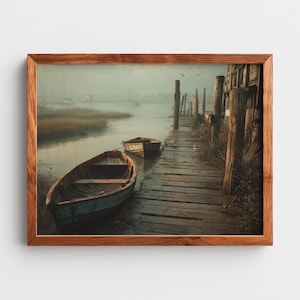 Puede incluir: Una impresión enmarcada de una escena costera con dos pequeños botes cerca de un muelle de madera. Los botes están en primer plano, con una vía fluvial brumosa y veleros distantes en el fondo. La obra de arte está en un marco de madera.