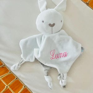 Personalised white bunny baby comforter embroidered with Luna in light pink thread. Baby comforter in is a cot.