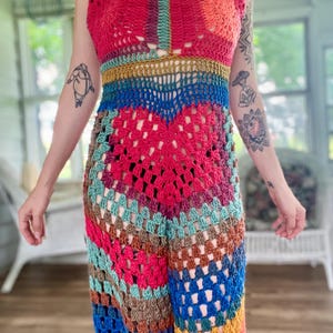 Puede incluir: Un mono halter de ganchillo hecho a mano y colorido. La prenda presenta una vibrante mezcla de tonos rojos, azules, naranjas y verdes. El diseño calado y el cuello halter crean una estética bohemia. El mono es una prenda de una sola pieza.