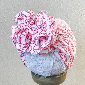 May include: White baby headband with a red and white baseball print and a white lace trim.