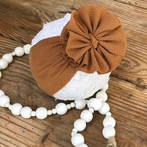 Peut inclure: Un bandeau noué brun et blanc avec un grand nœud brun. Le bandeau est sur une surface en bois avec une guirlande de perles blanches.