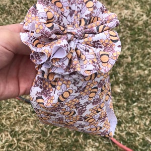 May include: A white headband with a ruffled design featuring a repeating pattern of bees and honeycombs. The headband is made of a soft, stretchy fabric.