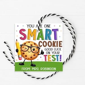 May include: A square gift tag with a cartoon cookie character wearing glasses and holding a pencil. The tag reads "YOU ARE ONE SMART COOKIE GOOD LUCK ON YOUR TEST!" and "FROM: MRS. ROBINSON". The tag is decorated with colorful stars and a green border.