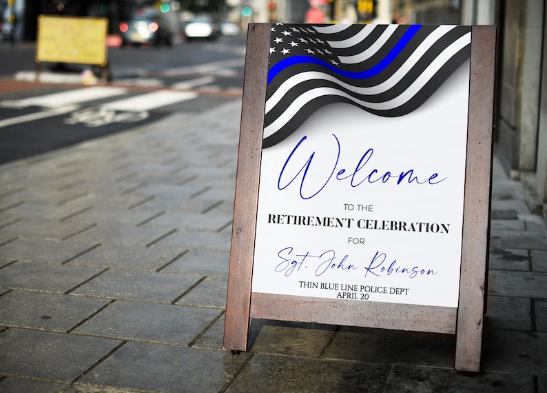 May include: A wooden A-frame sign with a white background and a blue and black American flag with a blue line. The sign reads "Welcome to the Retirement Celebration for Sgt. John Robinson Thin Blue Line Police Dept April 20".
