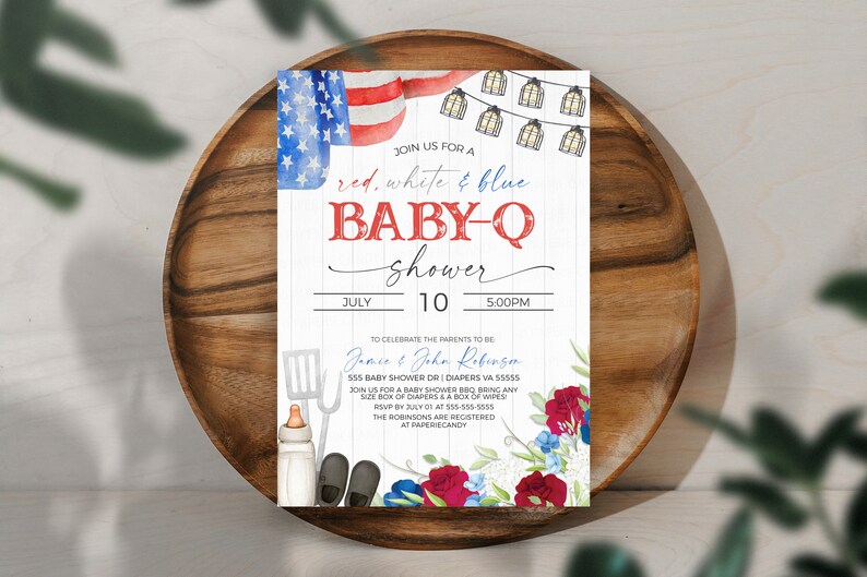 May include: Red, white, and blue baby shower invitation with a watercolor American flag, string lights, and floral accents. The invitation reads "Join us for a red, white & blue baby-q shower" with the date and time of the event. The invitation also includes the names of the parents-to-be, Jamce & John Robenzen, and their address.