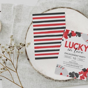 K&ouml;nnte beinhalten: Einladungen zur Verlobungsfeier mit Spielkarten-Motiv. Eine Karte hat rot-schwarze Streifen, die andere den Text "Lucky in Love" und Spielkarten-Grafiken. Die Einladungen liegen auf einer wei&szlig;en Holzoberfl&auml;che.