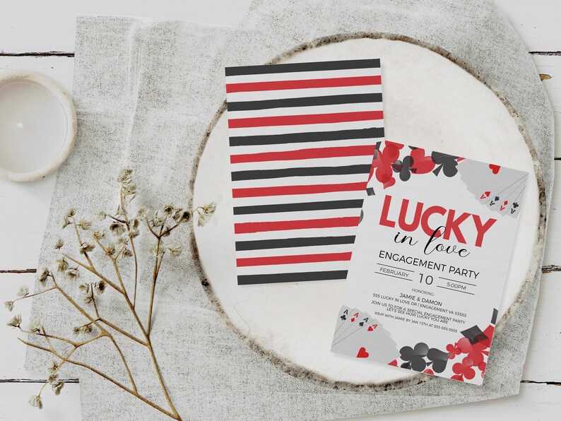 K&ouml;nnte beinhalten: Einladungen zur Verlobungsfeier mit Spielkarten-Motiv. Eine Karte hat rot-schwarze Streifen, die andere den Text "Lucky in Love" und Spielkarten-Grafiken. Die Einladungen liegen auf einer wei&szlig;en Holzoberfl&auml;che.