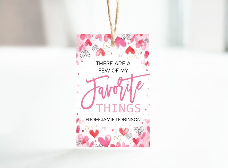 K&ouml;nnte beinhalten: Ein wei&szlig;er Geschenkanh&auml;nger mit einem rosa Aquarell-Herz-Muster. Der Text lautet "Das sind ein paar meiner Lieblingssachen. Von: Jamie Robinson."