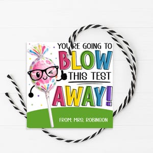 May include: A square gift tag with a colorful lollipop character wearing glasses and winking. The tag reads "You're going to blow this test away!" with the name "Mrs. Robinson" at the bottom. The tag is tied with black and white twine.