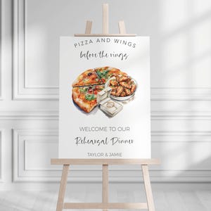 May include: A white sign on a wooden easel with the text "Pizza and Wings before the rings". The sign features a watercolor illustration of pizza, chicken wings, and a ring box. The text "Welcome to our Rehearsal Dinner" is also displayed.