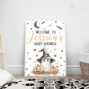 K&ouml;nnte beinhalten: Ein wei&szlig;es Schild mit schwarzem Rand und einem niedlichen Geist, der einen Hexenhut tr&auml;gt. Das Schild lautet "Willkommen zu Jessicas Baby Shower" mit orangefarbenen Sternen und Flederm&auml;usen um den Text herum. Auf beiden Seiten des Geistes befinden sich zwei orangefarbene K&uuml;rbisse.