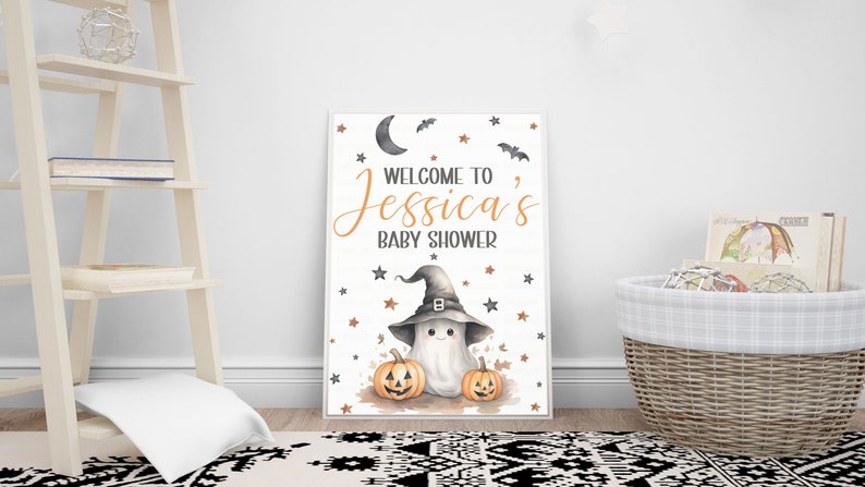 K&ouml;nnte beinhalten: Ein wei&szlig;es Schild mit schwarzem Rand und einem niedlichen Geist, der einen Hexenhut tr&auml;gt. Das Schild lautet "Willkommen zu Jessicas Baby Shower" mit orangefarbenen Sternen und Flederm&auml;usen um den Text herum. Auf beiden Seiten des Geistes befinden sich zwei orangefarbene K&uuml;rbisse.