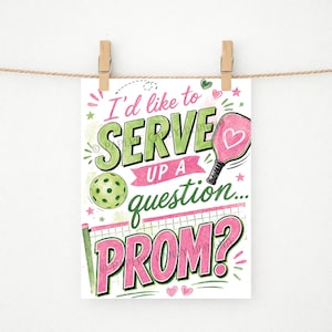 Può includere: Una stampa ad acquerello con il testo "I'd like to SERVE UP a question... PROM?" in verde e rosa. L'immagine include una racchetta da pickleball con un cuore, una pallina da pickleball e un disegno a rete. La stampa è tenuta da clip di legno su una corda.