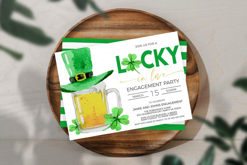 May include: Watercolor engagement party invitation with a green leprechaun hat, beer mug, and shamrocks. The invitation reads "Lucky in Love" with event details, set on a wooden tray.